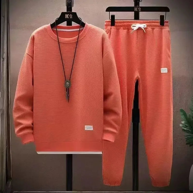 Coral tracksuit with sweatshirt and jogger pants on hangers against a neutral background